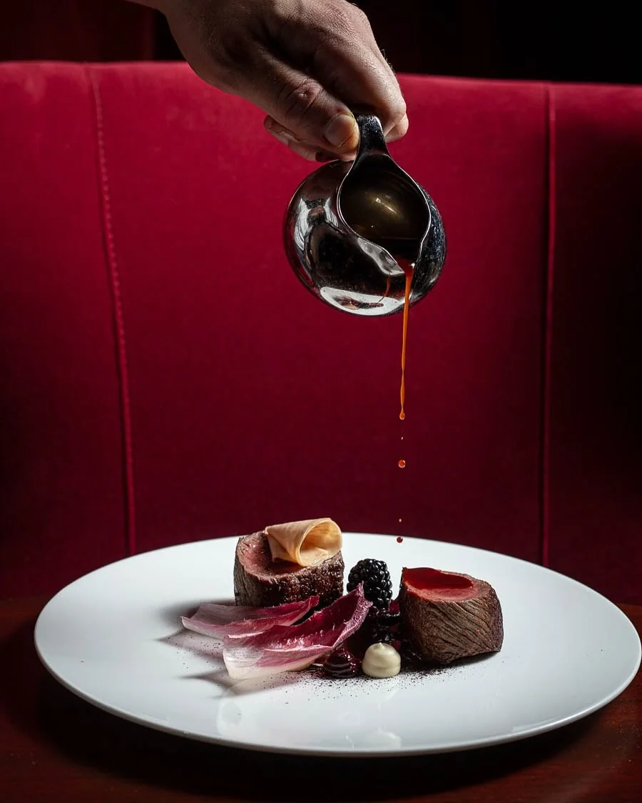 Sauce being poured beside a plated meat course